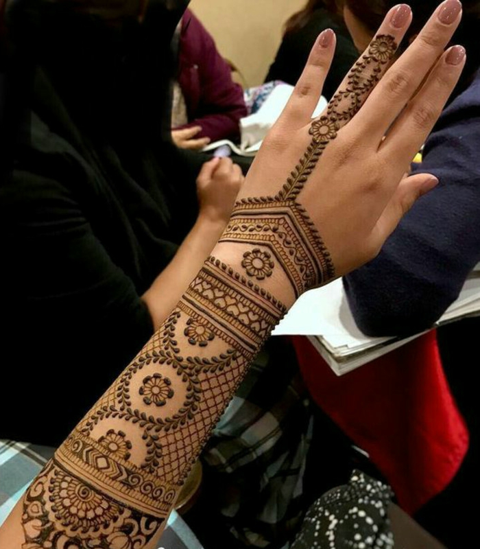 Tatuajes de mujeres en todo el brazo y el antebrazo con muchos pequeños adornos de color de henna, tatuaje de dedo anular