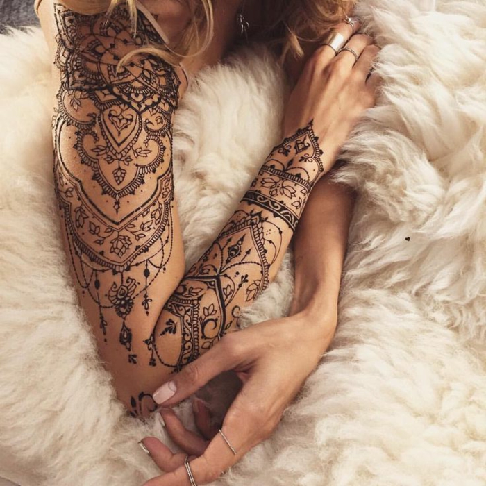 Жена с хубава ръка татуировка в черно, много малки елементи, цветни акценти, бяло одеяло, пръстени