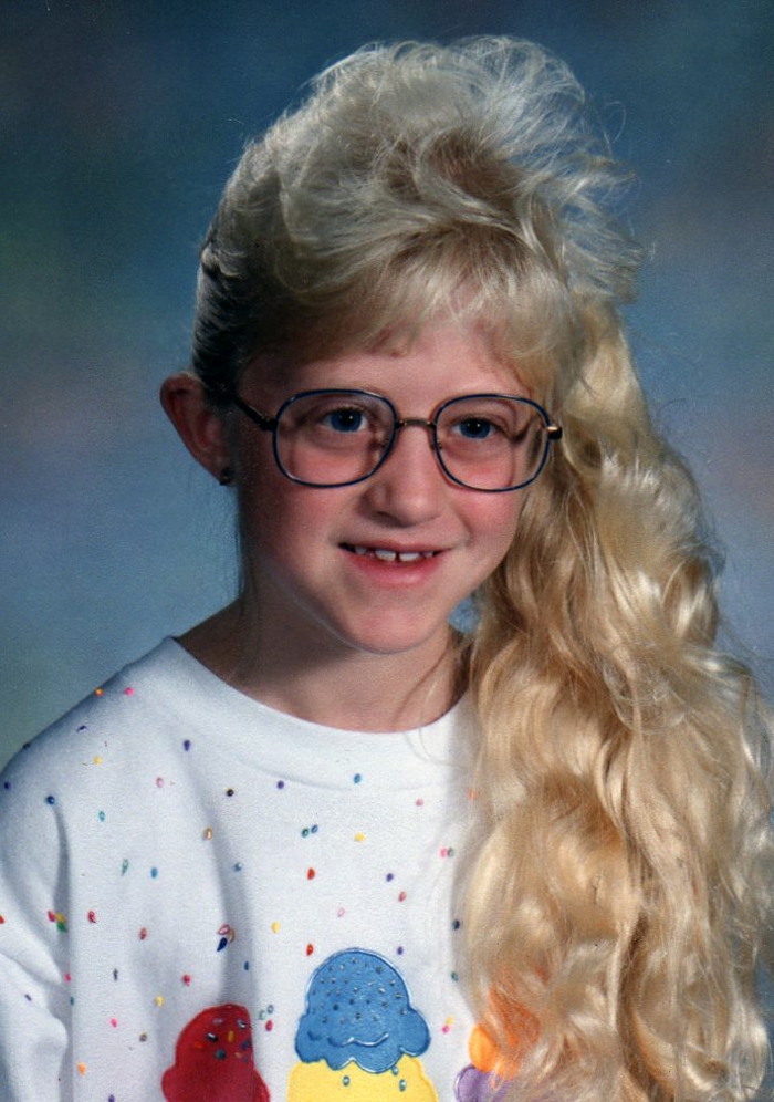 Момиче от 80-те години с опашка от коси, дълга руса вълнообразна коса, бяла блуза с печат, огромни очила за четене