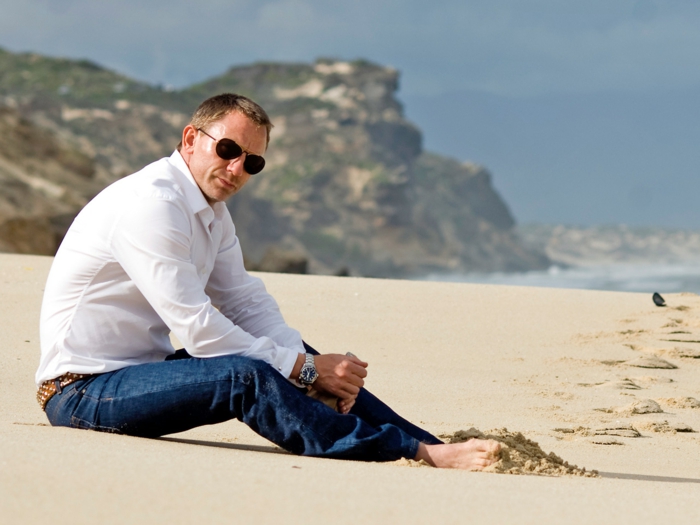 Даниел Craig на плажа дънки кафяв пояс бяла риза очила голяма прическа часовник