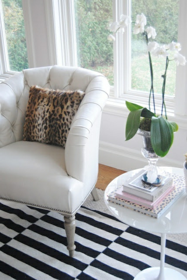 Salon avec un fauteuil blanc, des fleurs blanches, des coussins et une fenêtre