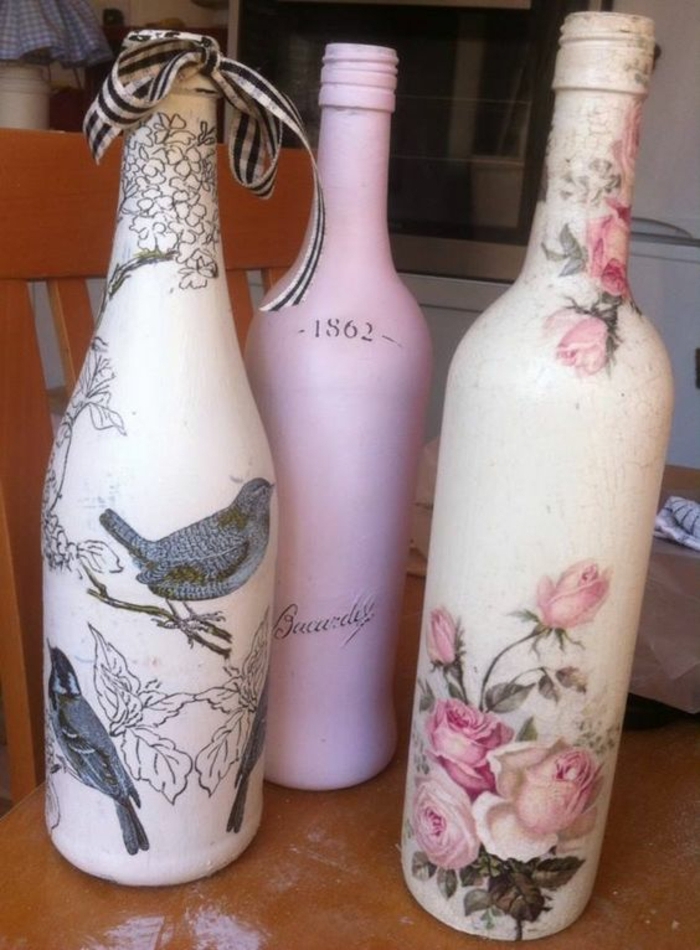 три бутилки със салфетки с розови цветя и сиви птици и сиво врабче