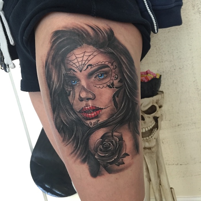 Pierna con un tatuaje de La Catrina con una mujer joven con labios rojos y ojos azules y una telaraña negra