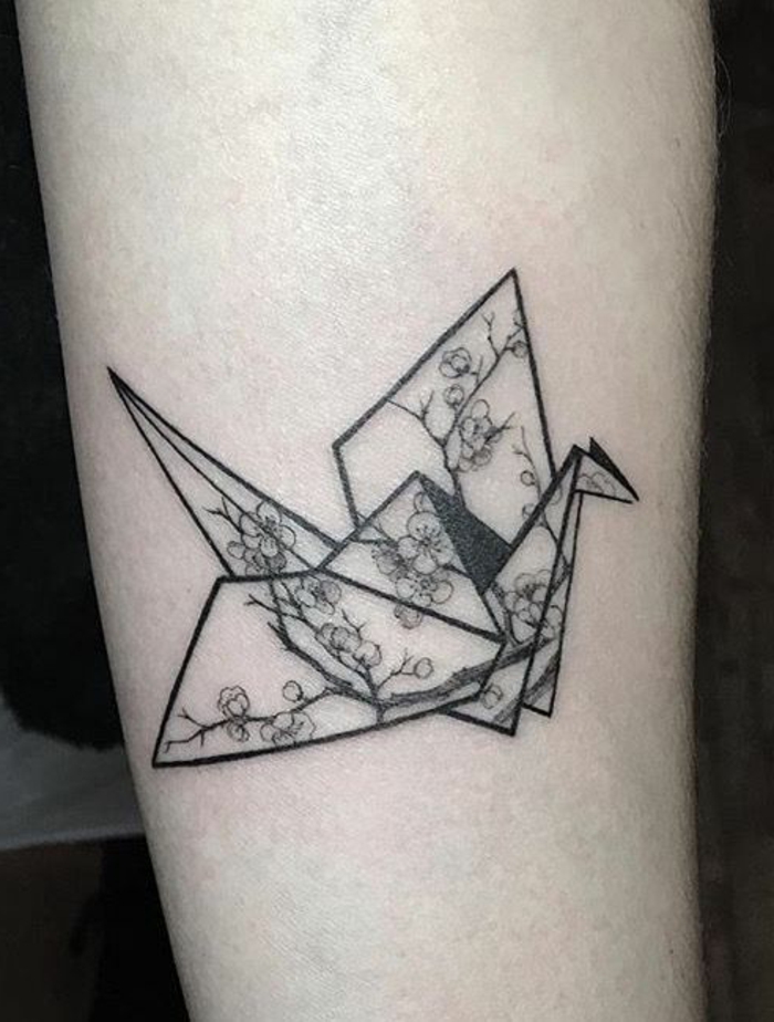 täältä löydät origami-tatuoinnin idean - lentävä musta origami-lintu pienillä valkoisilla kukilla