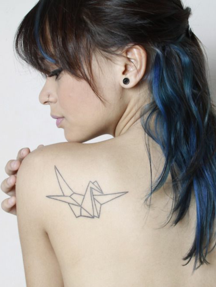 Tässä on nuori nainen, jolla on siniset hiukset ja pieni origami-tatuointi scapulassa - valkoinen lentävä origami-kyyhky