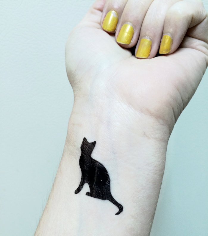 velika ideja za tetovažu mačke na zglobu - ovdje je ruka, žuti lak za nokte i malo crne mačke