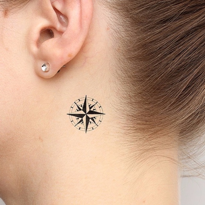 kompas tetovaža - mlada žena s tetovažom s crnim mini kompasom i malim naušnicama