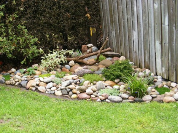 градински дизайн с декорация от малки камъни, зелени растения и дървесни клони