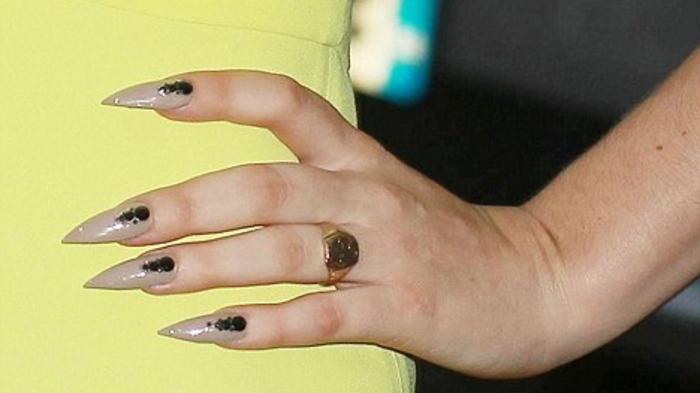 Τα μυτερά καρφιά της Lady Gaga μπεζ χρώματος των νυχιών μαύρο και χρυσό δαχτυλίδι κίτρινο φόρεμα