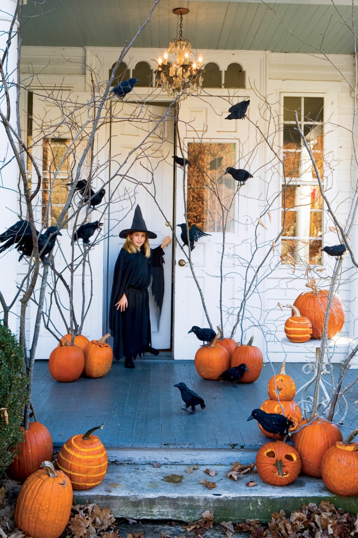 Halloween-díszítés, sok sütőtök és óriások, egy kis boszorkány az ajtó előtt, sütőtök faragása