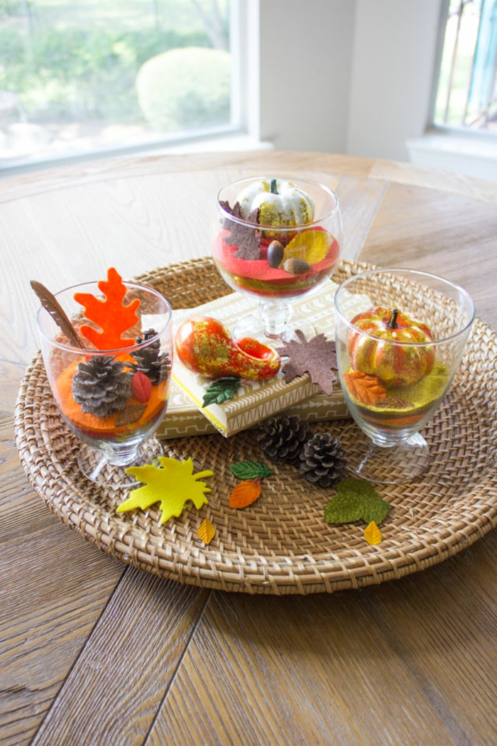 подреждане на масата есенно, плочи от ратан, конуси и малки тиквички в чаши, есенни нюанси