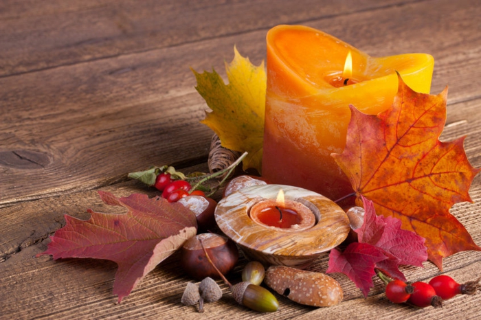 arregle la mesa de manera otoñal, castañas, bellotas, hojas de otoño y velas amarillas anaranjadas, matices otoñales