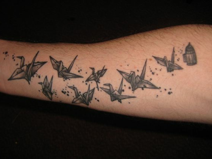 egy fekete ketrec és sok kis fekete repülő origami madár - egy origami tetoválás a kezére