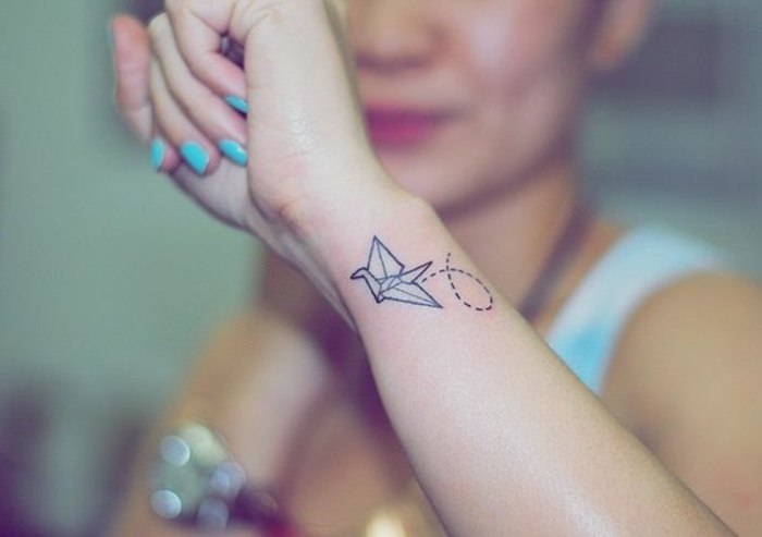 Τώρα σας παρουσιάζουμε μια από τις ιδέες μας σχετικά με τατουάζ ορταντί για τις γυναίκες - ένα πετούν λευκό όμορφο πουλί origami σε ένα χέρι με ένα μπλε βερνίκι νυχιών