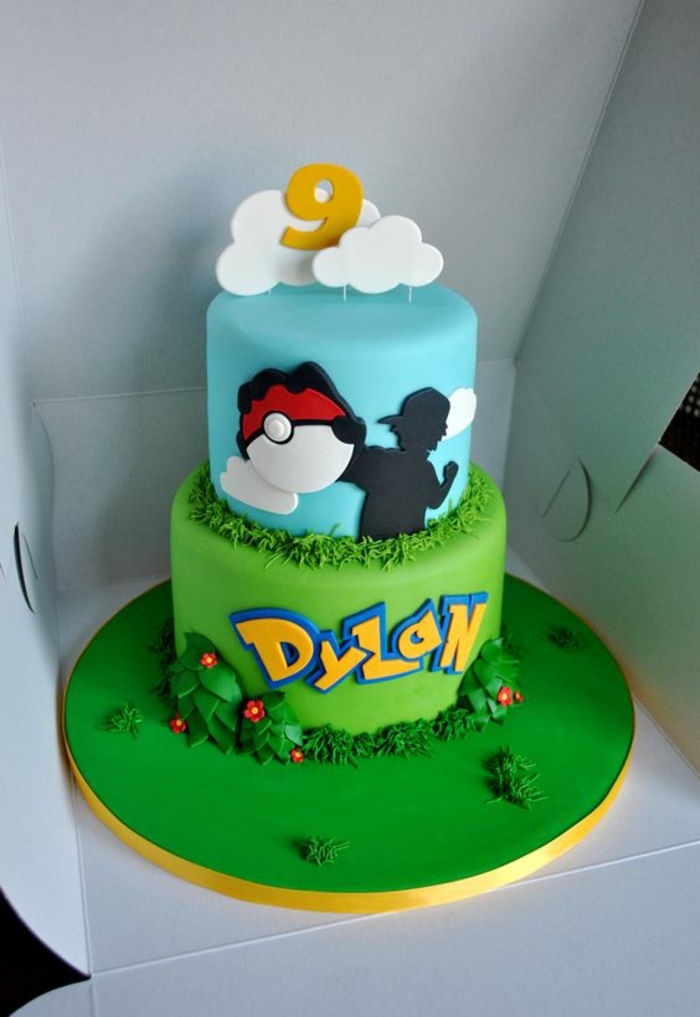 gâteau de pokemon de deux étages avec des nuages, des fleurs et un pokeball rouge et de l'herbe