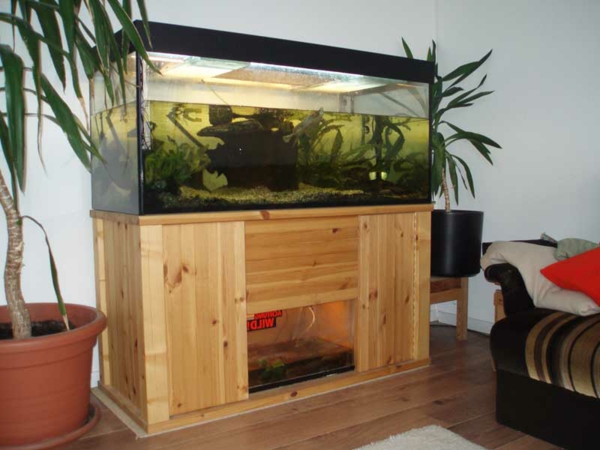 Две големи зелени растения като декорация до аквариум с дървен шкаф