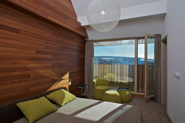chambre à coucher avec mur en bois et verre mur oreillers verts et lustre rond