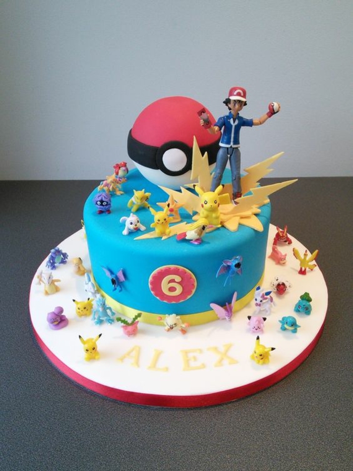una tarta de pokemon azul con destellos amarillos, una pokebola roja, pequeños seres pokemon diferentes, pikachu, chico con una gorra roja