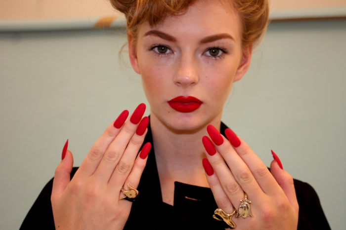gel καρφιά μυτερά μοντέλο γυναίκα με κόκκινα χείλη και κόκκινο μακρύ τζελ νύχια χρυσά δαχτυλίδια διακόσμηση ρετρό στυλ make-up χτένισμα