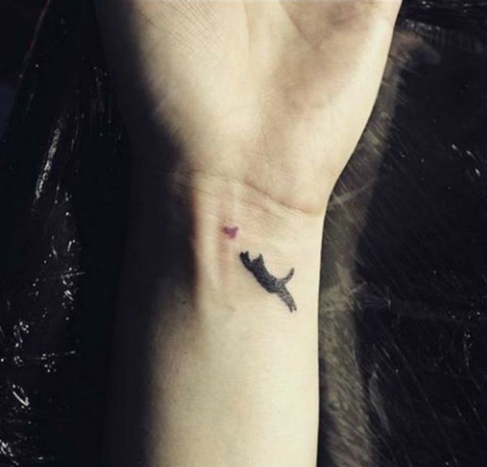 Това е ръка с малка татуировка с черна котка и птица - идея за татуировка на китката