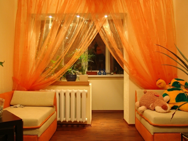 dnevni boravak s prozirnim zavjesama u narančastim plišanim igračkama pored nje