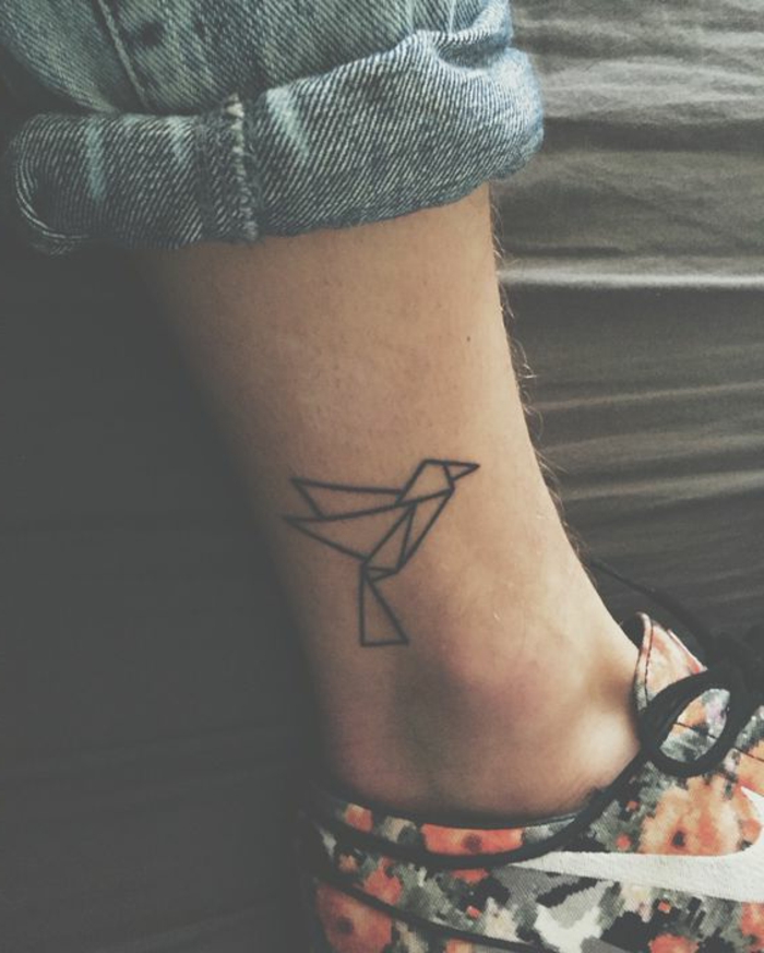 ένα πόδι με ένα μικροσκοπικό τατουάζ μίνι με μοτίβα origami - ένα μικρό μαύρο που φέρουν πουλί origami