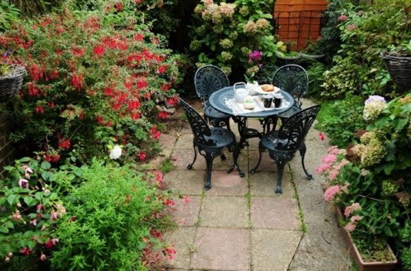 hermoso jardín con muchas flores de colores y una pequeña mesa de café con cuatro sillas