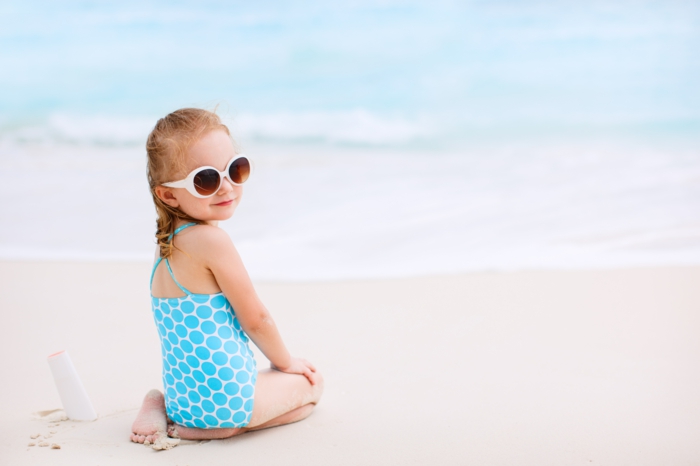 Малко момиче с бутилка слънце крем на тропически плаж