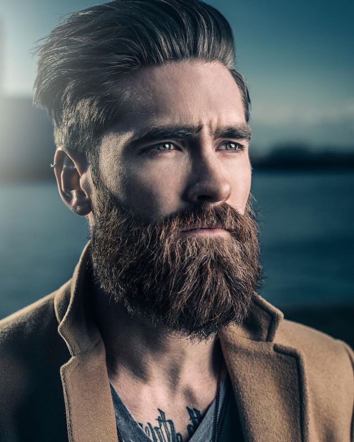 елегантно облечен мъж с брада, пиърсинг на спирала, кафяво палто, вода