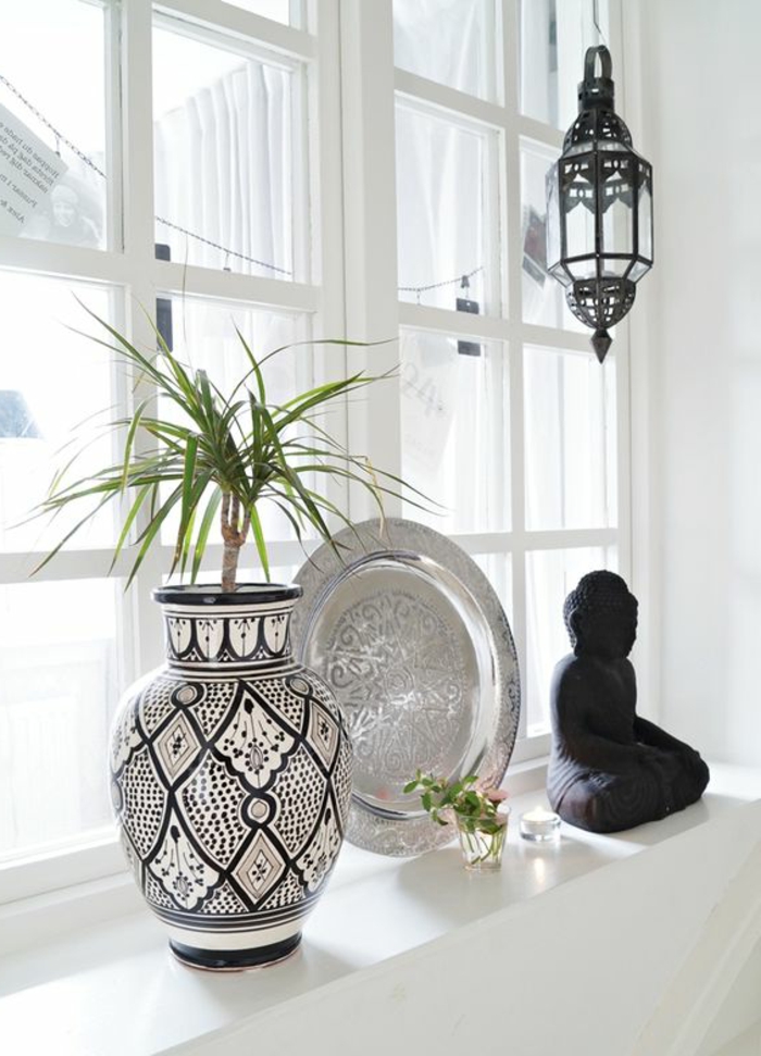 Dekoriranje prozora sa suvenirima: ukrasna keramička cvjetna vaza, metalna ploča, Buddah kip od drva