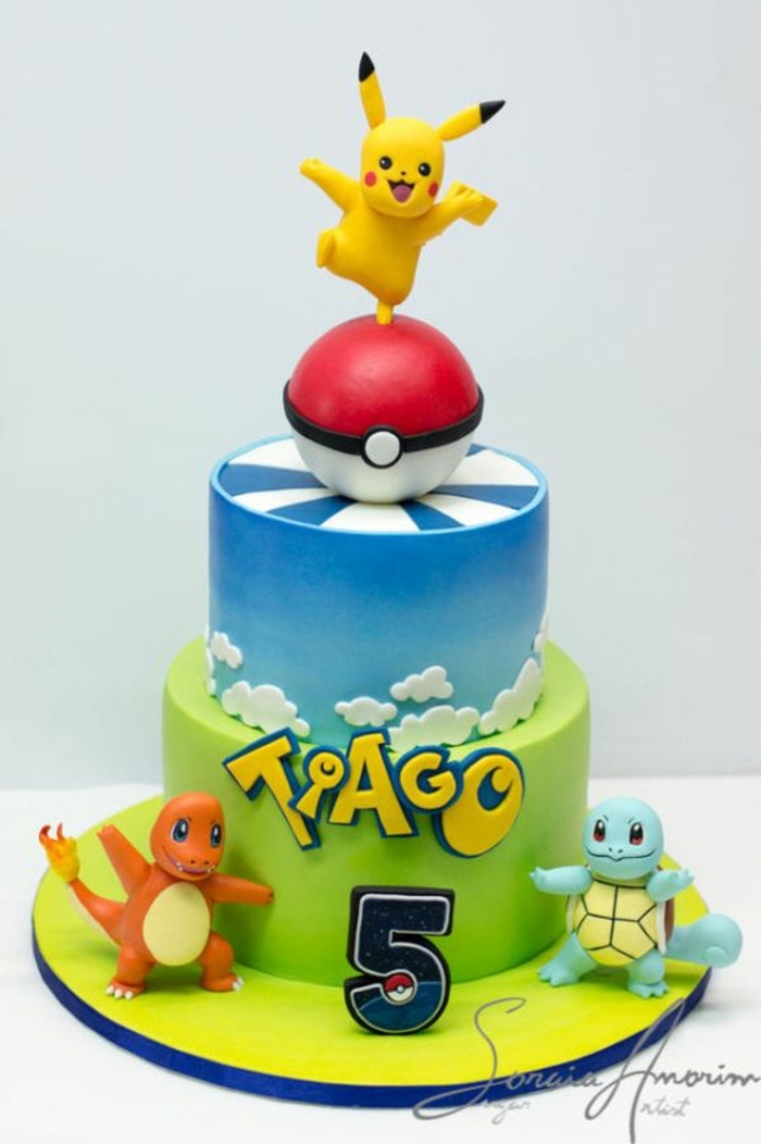 Une idée pour une tarte de deux étages avec une pokeball rouge, des nuages, des titres jaunes, trois petits êtres pokémon et pikachu